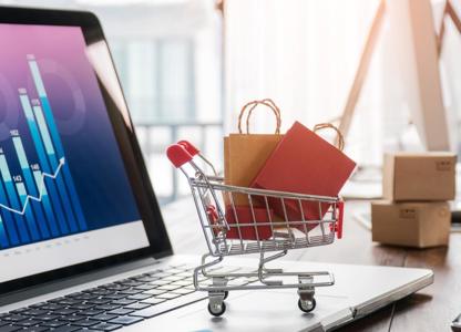Small shopping trolley graphic filled with packages placed on a laptop displaying data charts