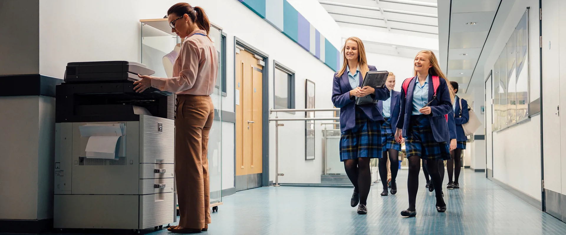 School teacher using a photocopier, children in corridor, smiling